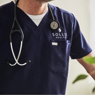 Image of a doctor wearing blue scrubs with an embroidered Sollis Health logo, and a stethoscope around their neck.