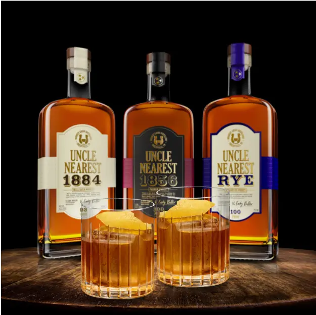 Three glass bottles of Uncle Nearest premium whiskey on a wood tabletop, with two glass tumbler glass filled with whiskey.