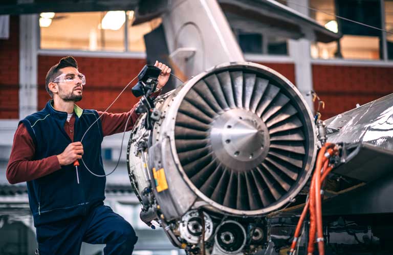 Aviation technician inspecting large commercial jet engine in hangar
