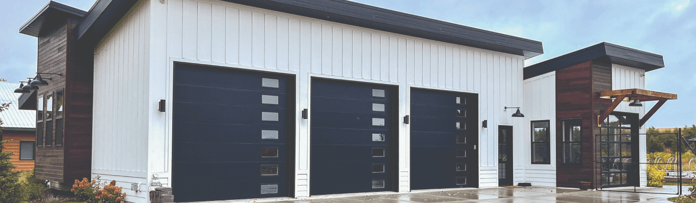 Modern white building with three dark garage doors and wood accents
